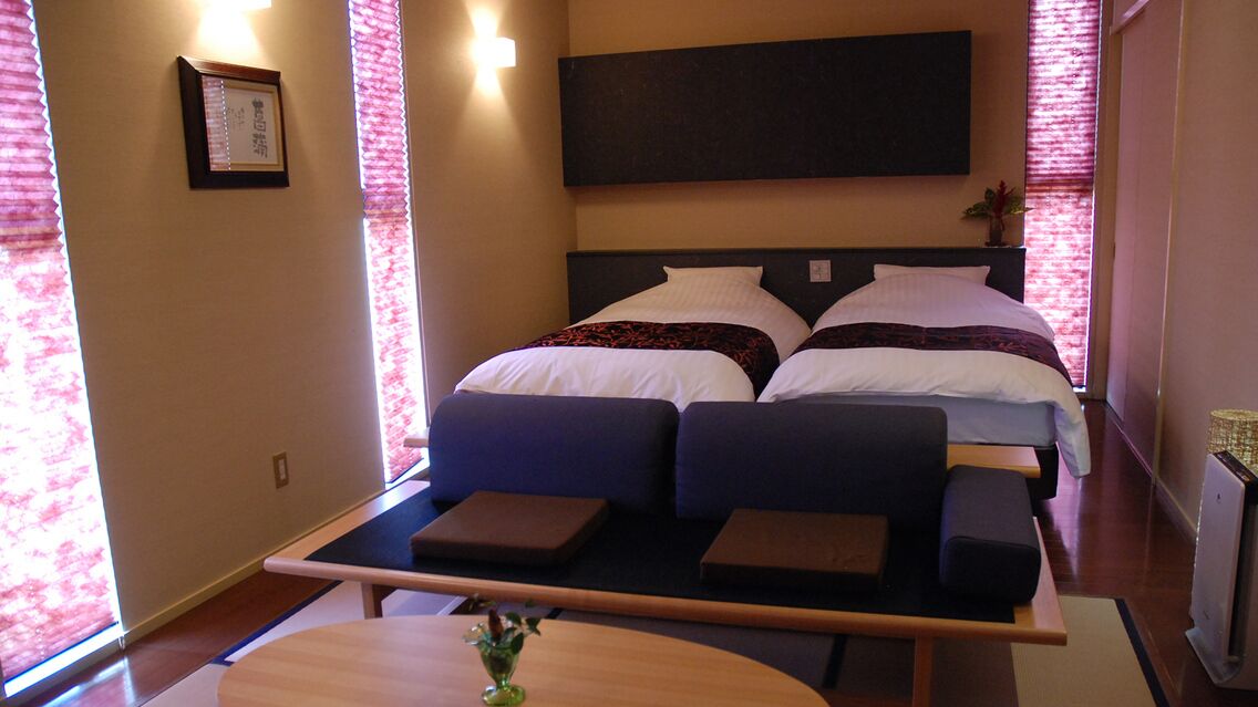 Ein Hotelzimmer mit Bett, Sofa, kleinem Tisch und Fenster mit Jalousien.