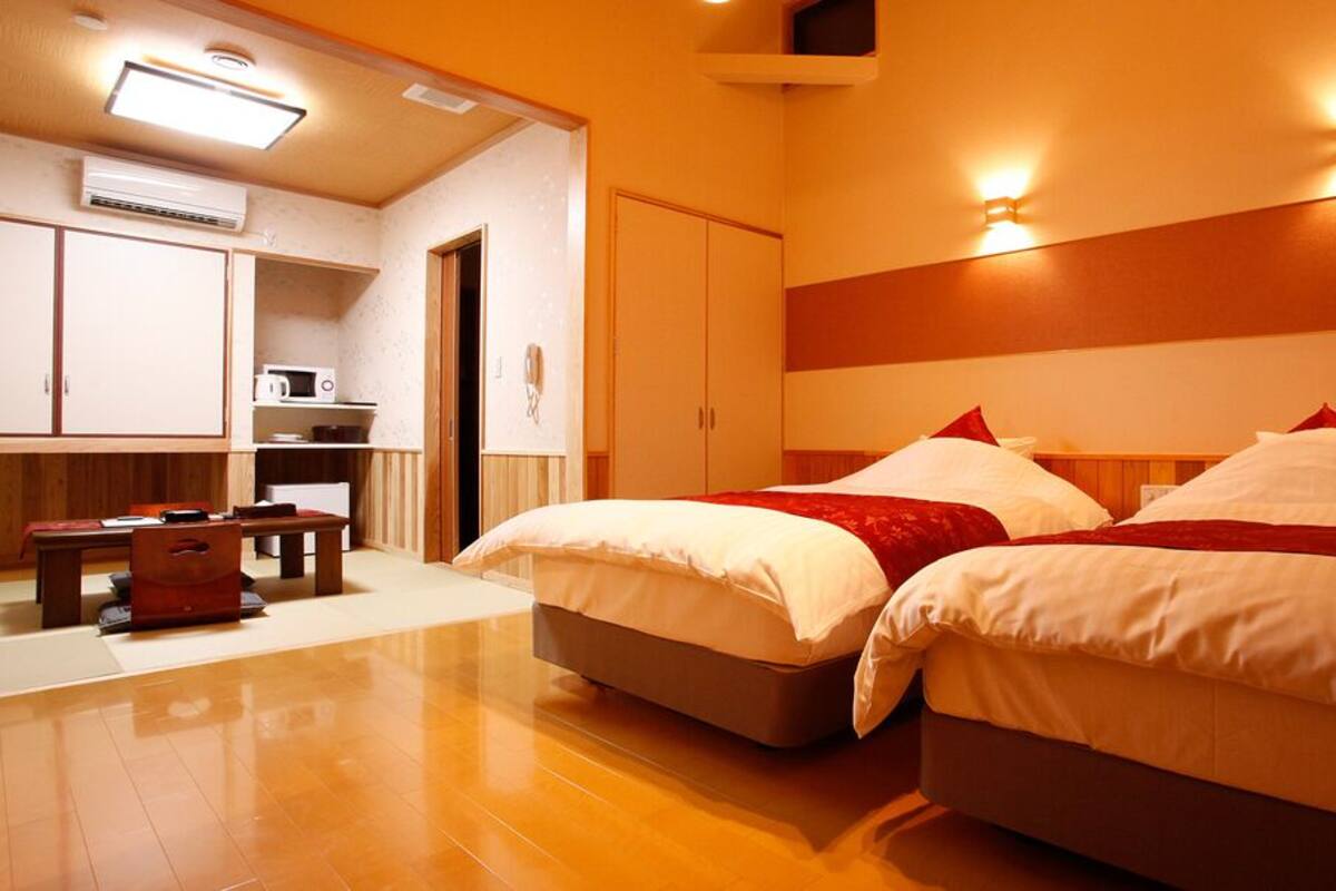 A hotel room with two beds, a small table, a microwave, and a wardrobe.