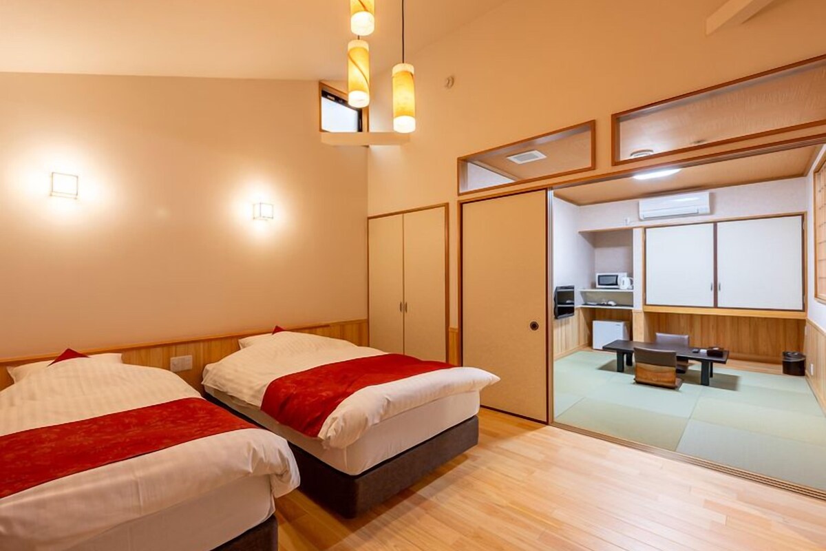 Ein Hotelzimmer mit zwei Betten, einer Küchenzeile und einer Schiebetür zum Badezimmer.