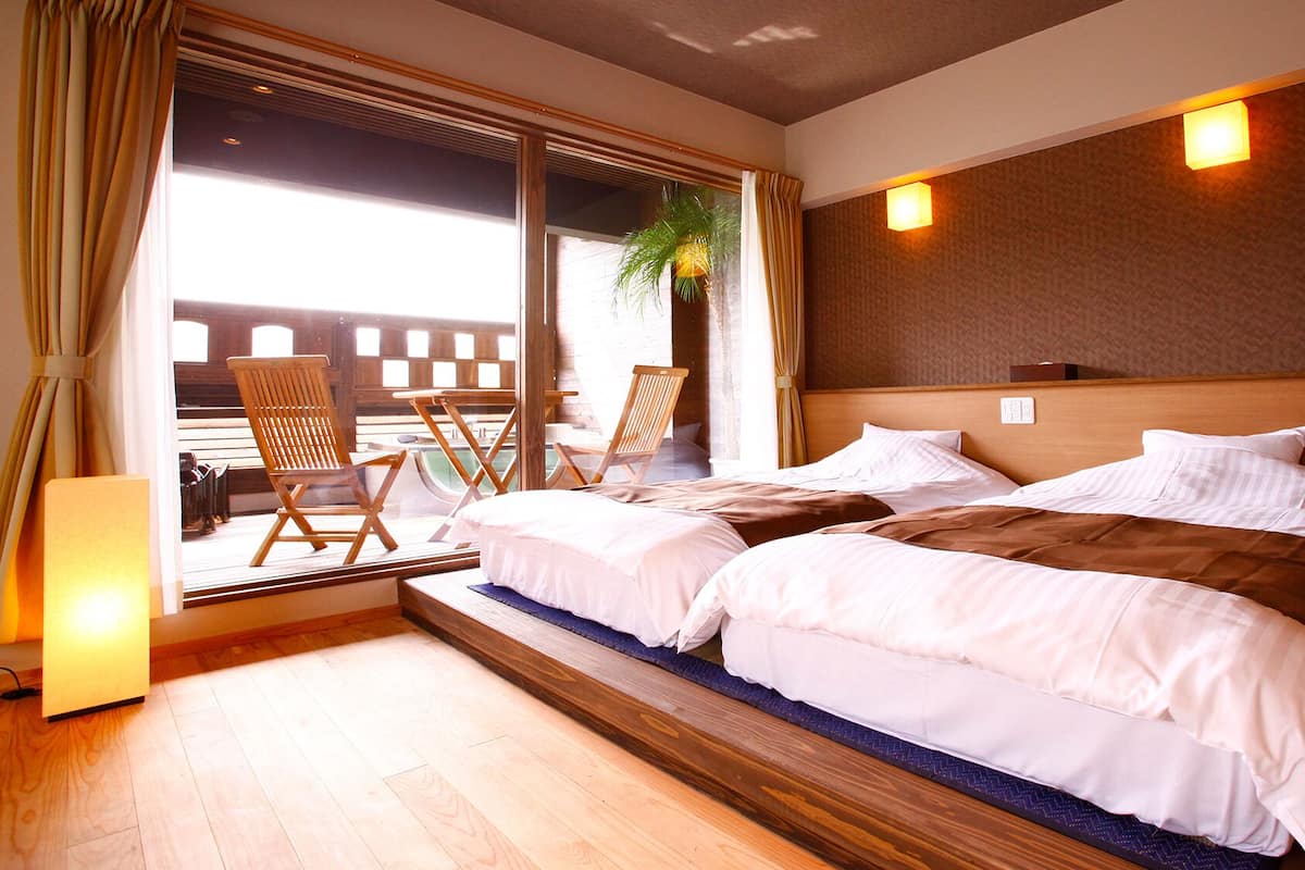 Habitación de hotel con una cama grande, dos sillas, una mesita y vistas a un edificio a través de una ventana.