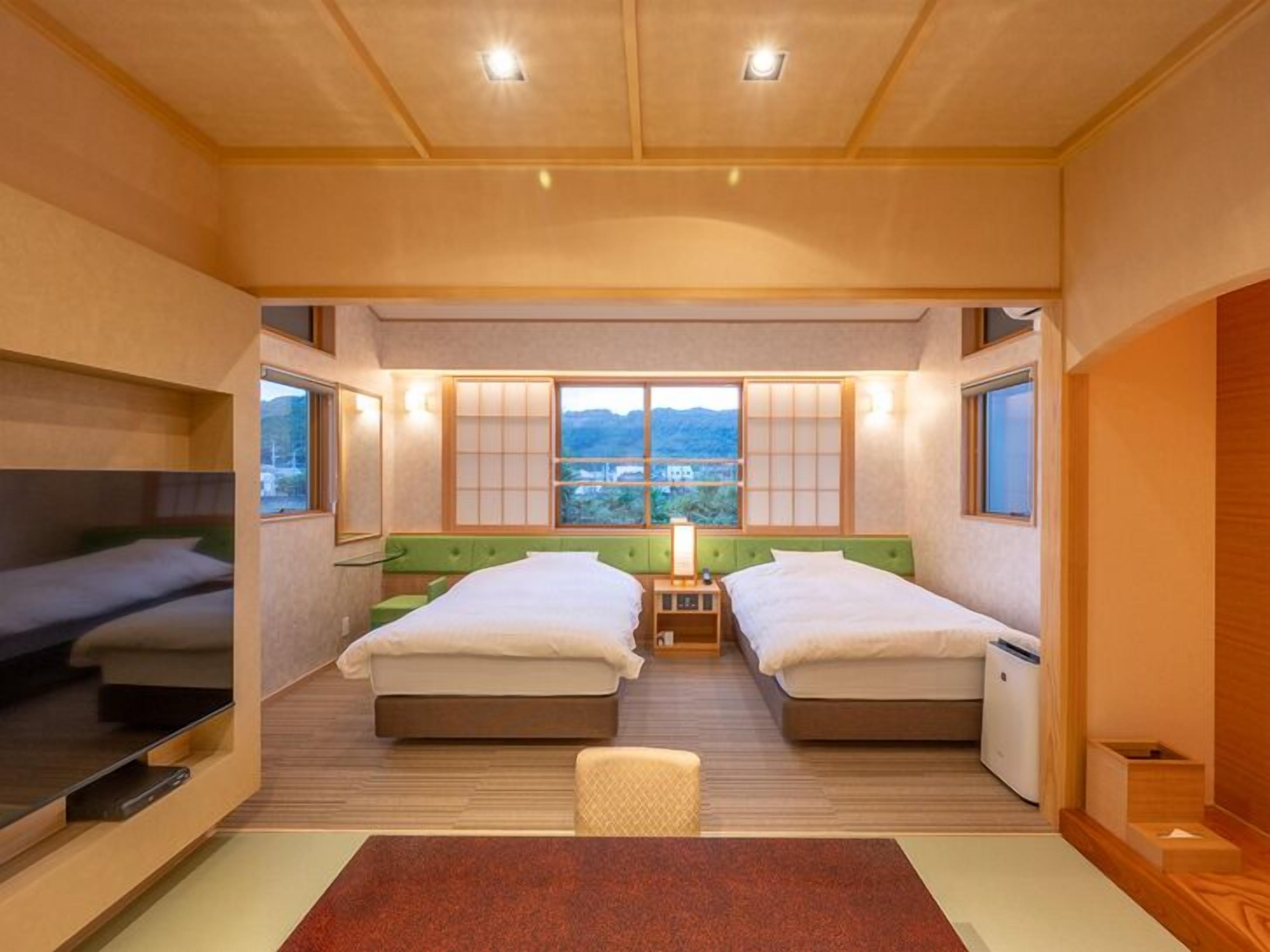 Ein kleines Hotelzimmer mit zwei Betten, einem Tisch und Blick ins Freie.