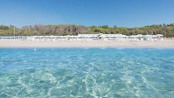 Ein Hotel am Strand mit klarem, blauem Wasser, einem Sandstrand und einer Reihe weißer Gebäude mit Sonnenschirmen.