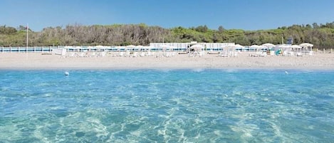 Un hotel frente a la playa con aguas cristalinas, una playa arenosa y una hilera de edificios blancos con sombrillas.
