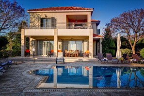 A two-story building with a swimming pool, outdoor seating, and a view of the surrounding landscape. - Niki Villa (Argaka)