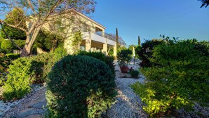 A two-story building with a balcony, surrounded by well-maintained gardens and a gravel path. - Niki Villa (Argaka)