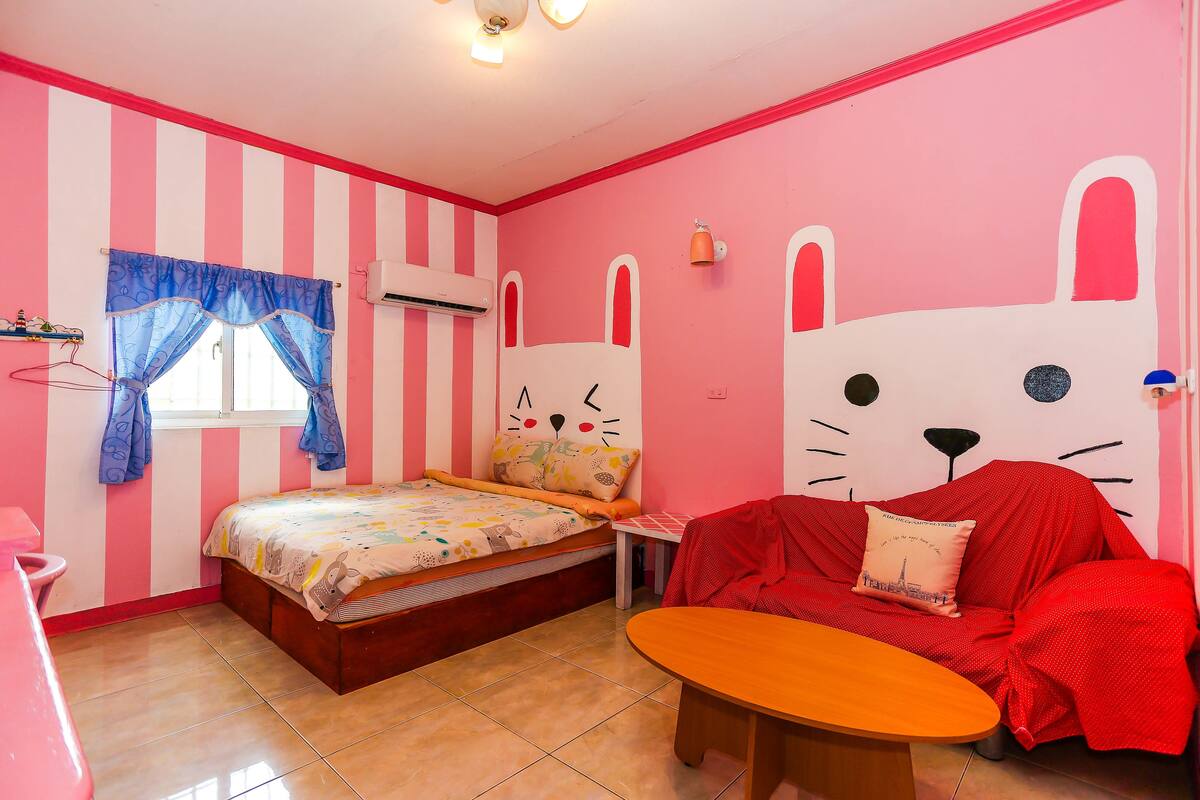 Una habitación con una cama, un sofá rojo, una mesita y una ventana con cortinas.