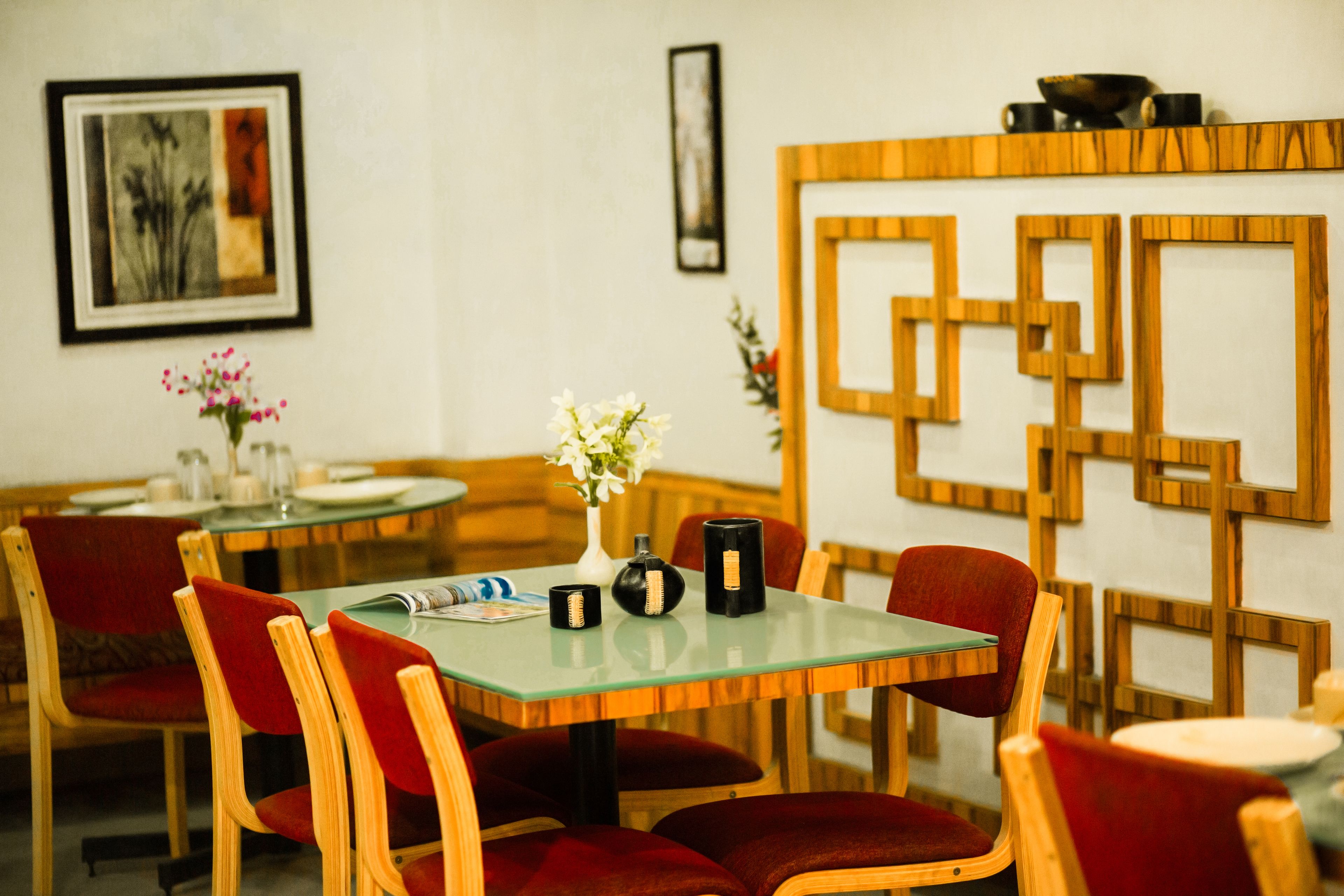Un comedor con sillas de madera y una mesa de vidrio, un panel decorativo de madera en la pared, y un jarrón con flores sobre la mesa.