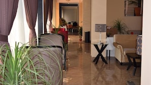 Un moderno vestíbulo de hotel con piso pulido, un área de descanso con sofá y sillones, y un comedor al fondo.
