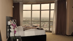 Una habitación de hotel con un ventanal grande, una cama, una mesita de noche y una planta en maceta.