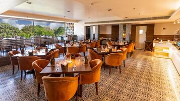 Un restaurante con varias mesas y sillas, un suelo con diseño y amplios ventanales que ofrecen vistas a zonas verdes.