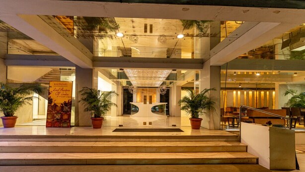 A modern hotel lobby with a central reception desk, potted plants, and a staircase leading to upper floors. - Hotel Hardeo (Nagpur)