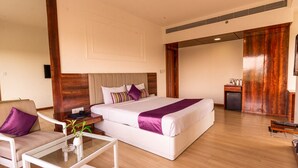 A hotel room with a large bed, a sofa, a small table, and a desk. - Hotel Hardeo (Nagpur)
