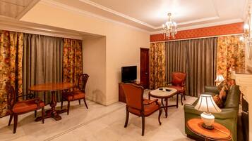 A hotel room with a dining area, a television, a green sofa, and a chandelier.