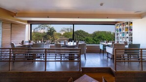 A spacious dining area with modern furniture and a large window offering a view of greenery. - Hotel Hardeo (Nagpur)