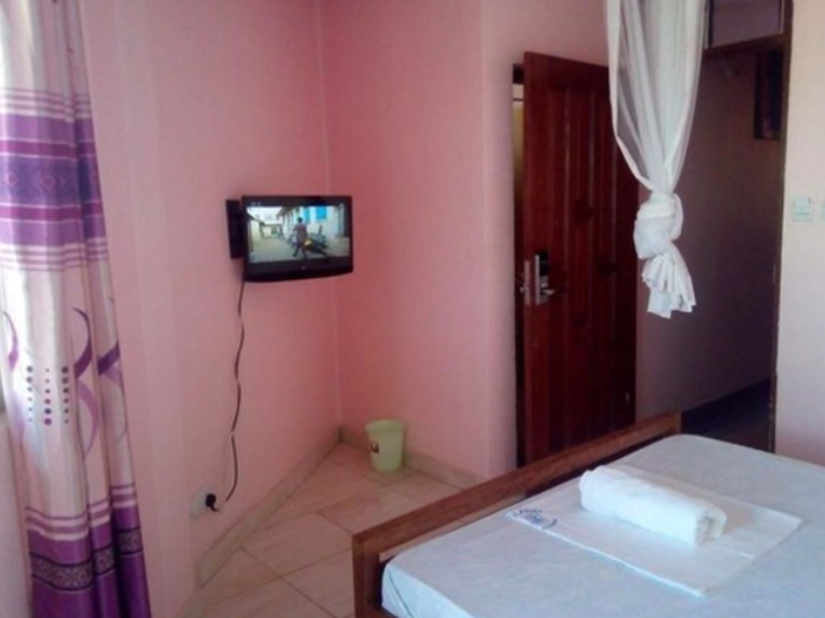 Una habitación con una cama, un televisor montado en la pared, una puerta de madera y una cortina.