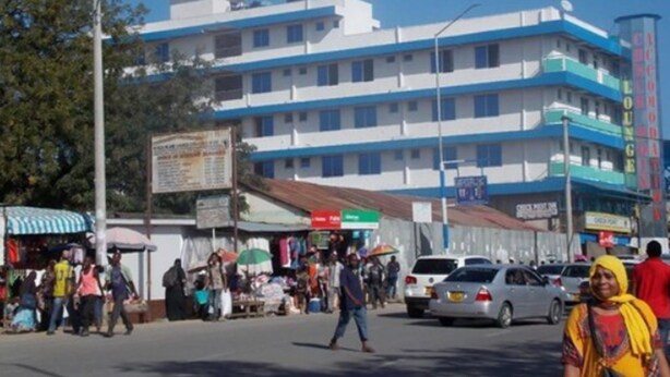 A multi-story building with a blue and white facade, a visible signboard, and a street with pedestrians and vehicles. - Check Point Inn Mombasa (Mombasa)