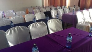 A conference room with rows of white chairs, purple tablecloths, and water bottles on the tables. - Check Point Inn Mombasa (Mombasa)