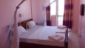 A single bed with a canopy, a bedside table, and a window with curtains. - Check Point Inn Mombasa (Mombasa)