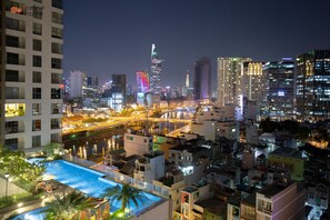 A cityscape at night with illuminated buildings, a river, and a swimming pool area with lights. - Celine Home Millenium (Ho Chi Minh City)