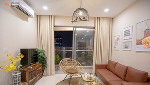 A modern living room with a sofa, a wicker chair, a round coffee table, and a TV on a wooden cabinet. - Celine Home Millenium (Ho Chi Minh City)