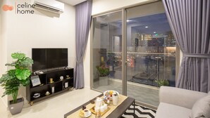 A modern living room with a flat-screen TV, a sofa, a coffee table with a tray of snacks, and a large window with curtains. - Celine Home Millenium (Ho Chi Minh City)