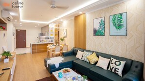 Un salon moderne avec un canapé vert foncé, une table basse agrémentée d’objets décoratifs et une cuisine en arrière-plan.