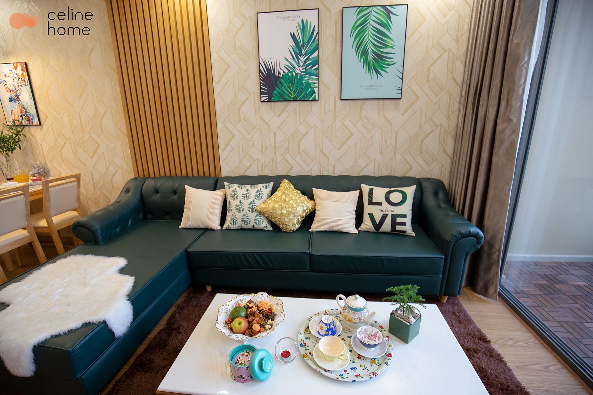 A cozy living room with a green sofa, decorative pillows, a coffee table with a floral tray, and framed artwork on the wall.
