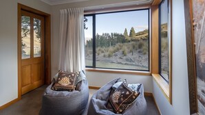 Habitación con un ventanal grande que ofrece vistas a un paisaje montañoso. Hay dos sillones orejeros grises con cojines decorativos.