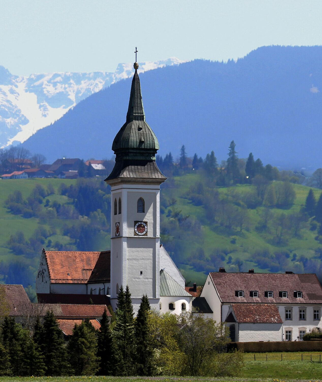 A church with a clock tower, surrounded by houses and a mountainous landscape.