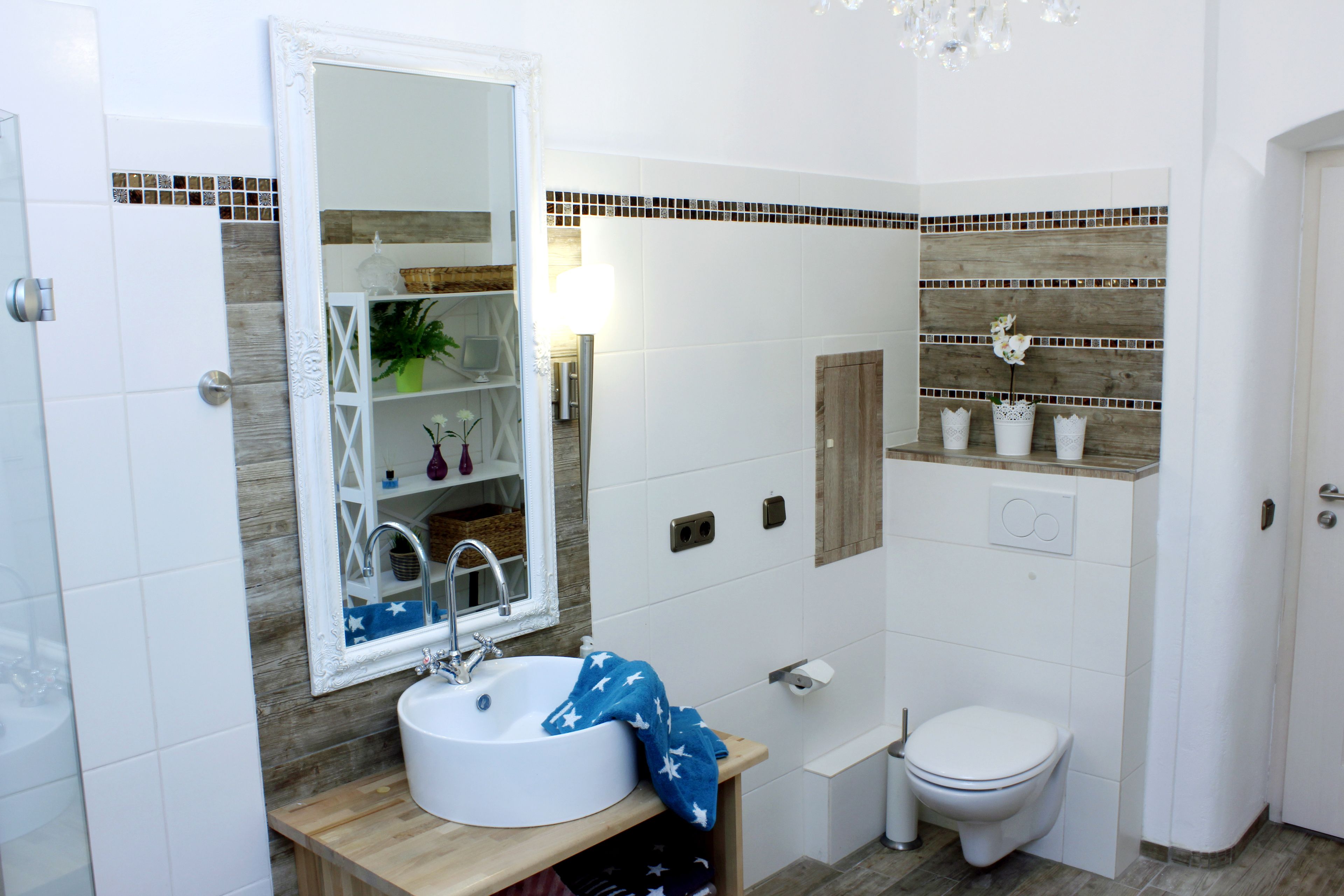 Ein Badezimmer mit einem weißen Waschbecken, einem Spiegel, einer Toilette und einem Ablagefach mit Pflegeprodukten.