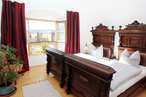 A bedroom with a large wooden bed, a window with a view, a potted plant, and a wooden dresser. - Ultra Alpes (Rottenbuch)