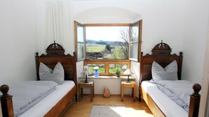 A bedroom with two wooden beds, a window with a view of the countryside, and a small desk with a lamp and a plant. - Ultra Alpes (Rottenbuch)