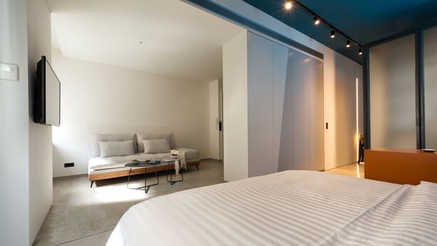 A modern hotel room with a large bed, a sofa, a small table, and a TV mounted on the wall. - Syntagma Square Modern Apartments (Athens)