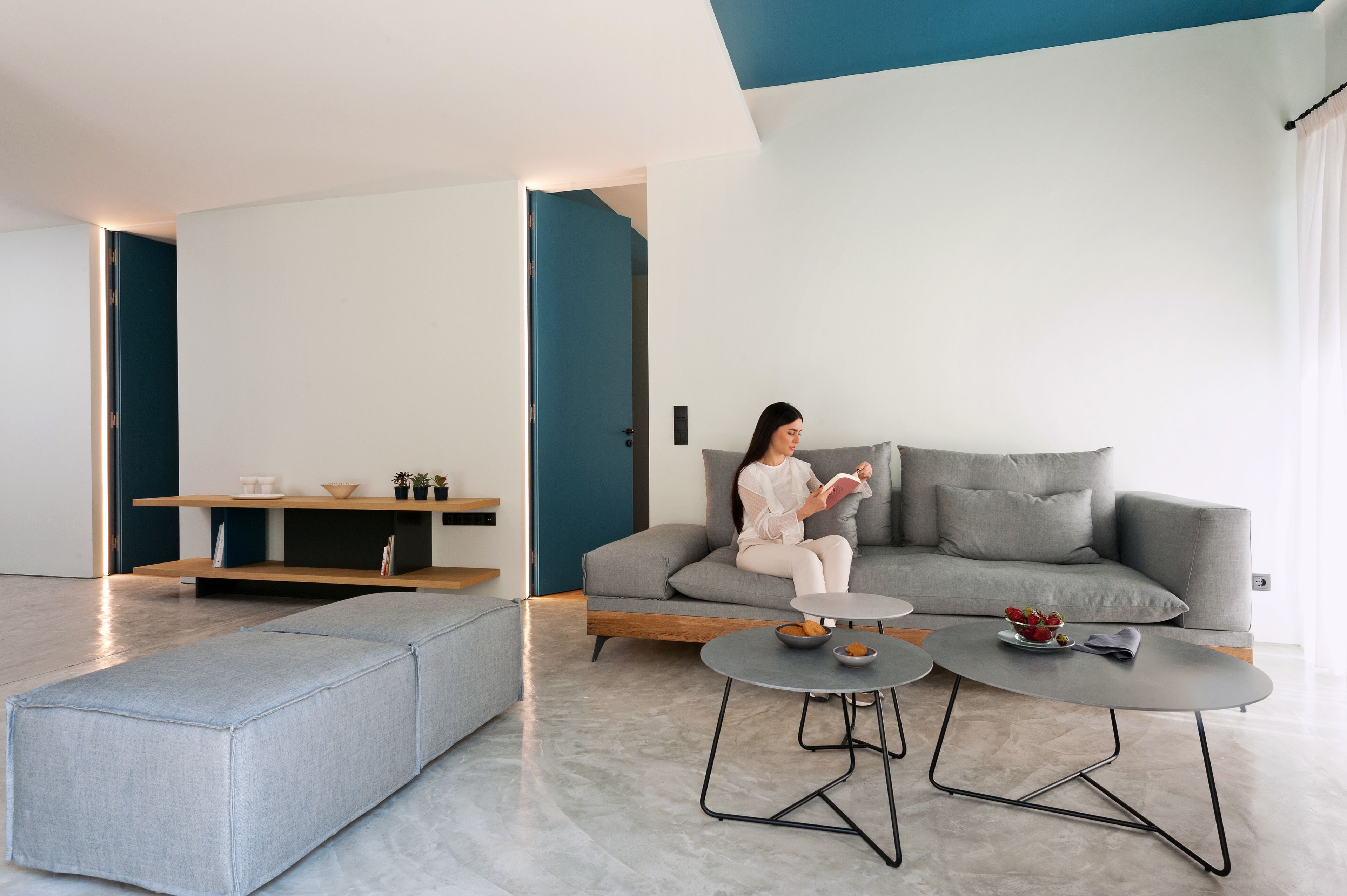 En moderne stue med en grå sofa, et rundt sofabord og en blå bænk.