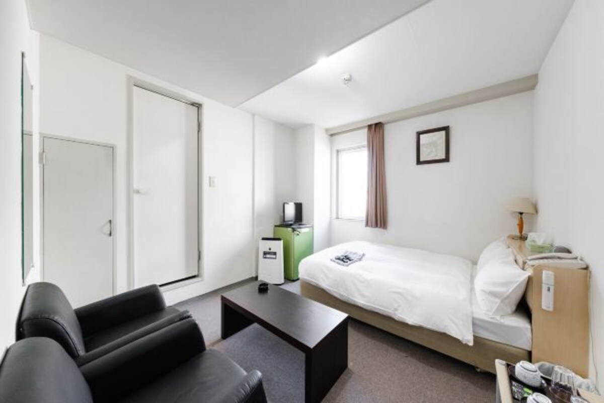 Una habitación de hotel compacta con cama, escritorio, silla, armario y televisor.