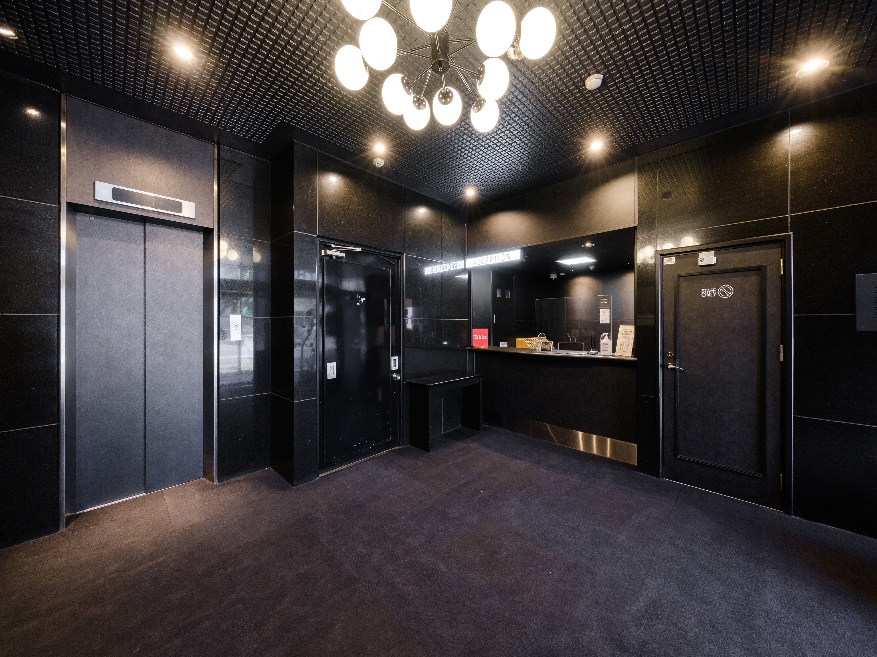 A modern reception area with a black and grey color scheme, a reception desk, and a sign indicating a staff-only door.