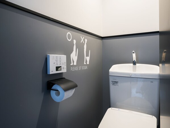 A modern bathroom with a toilet, a hand dryer, and a toilet paper dispenser.