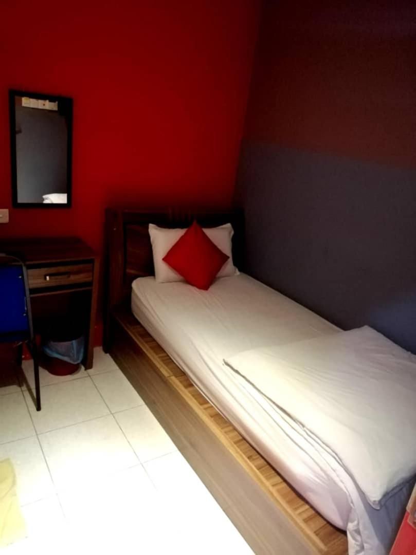 A single bed with a wooden headboard, a small desk with a chair, and a red wall.