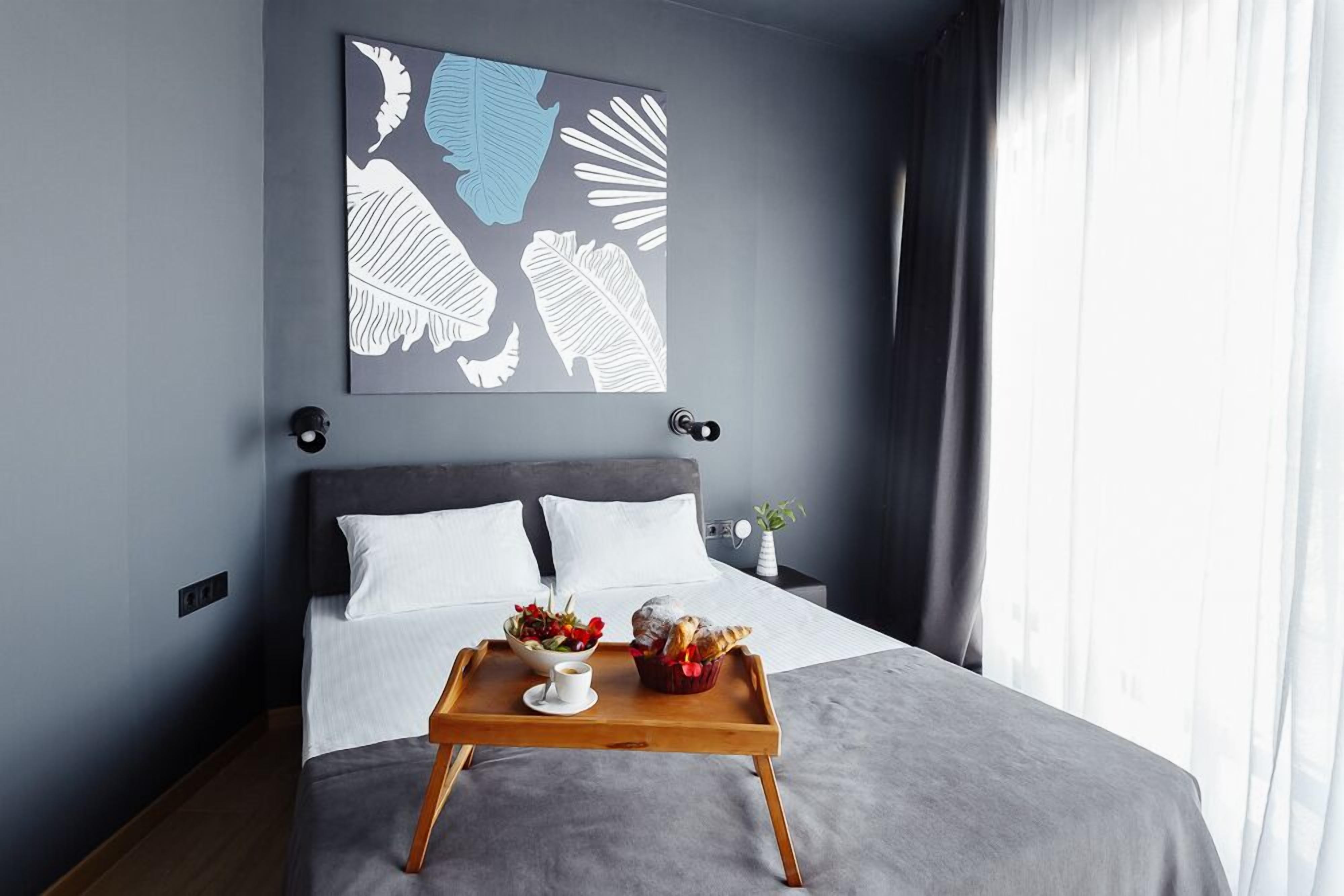 Quarto de hotel moderno com cama, bandeja de café da manhã, uma obra de arte na parede e janela com cortinas.