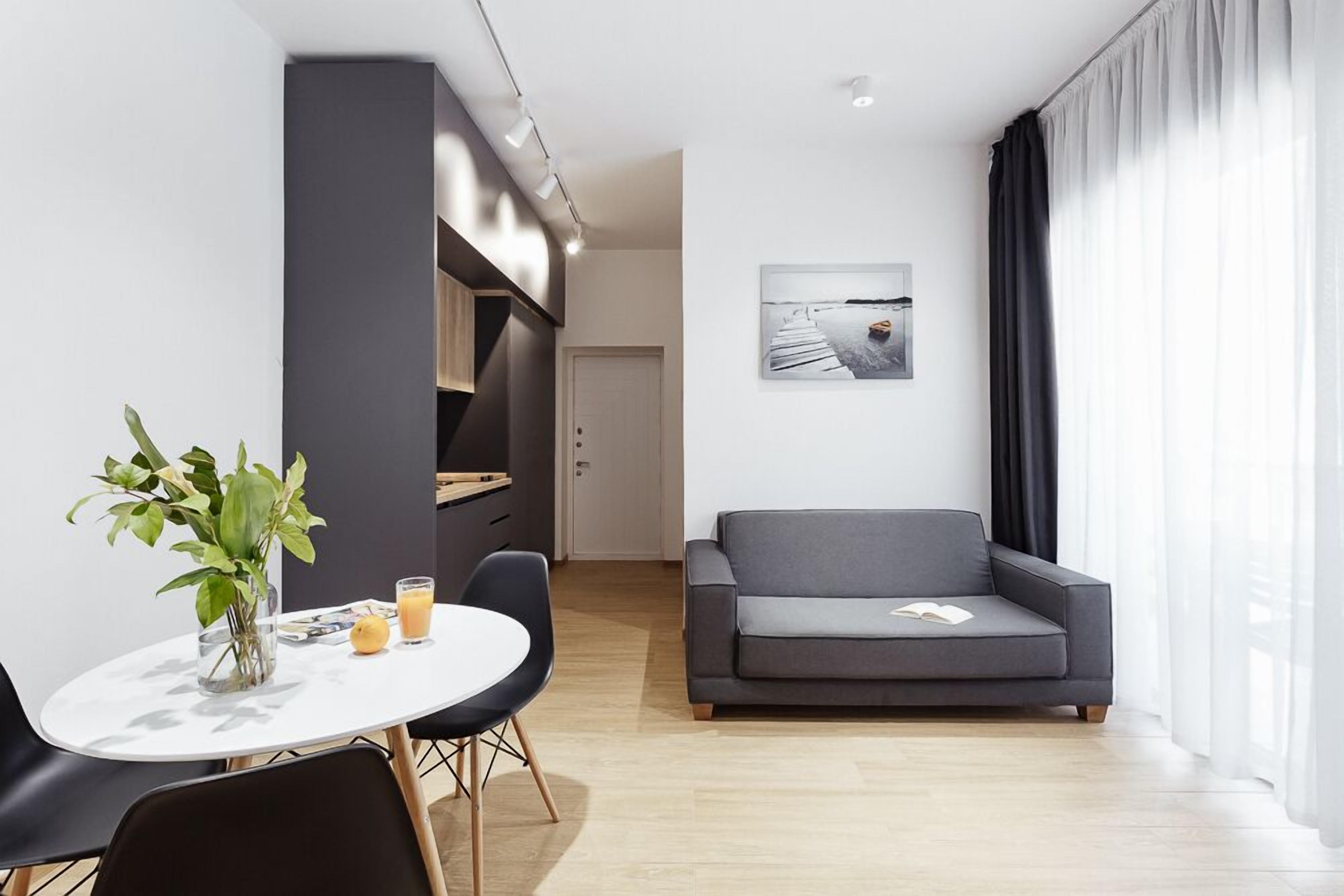A modern living room with a grey sofa, a dining table with chairs, a plant, and a framed picture on the wall.