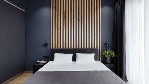 A modern bedroom with a dark blue wall, a wooden slatted ceiling, a black headboard, and a bedside table with a lamp.