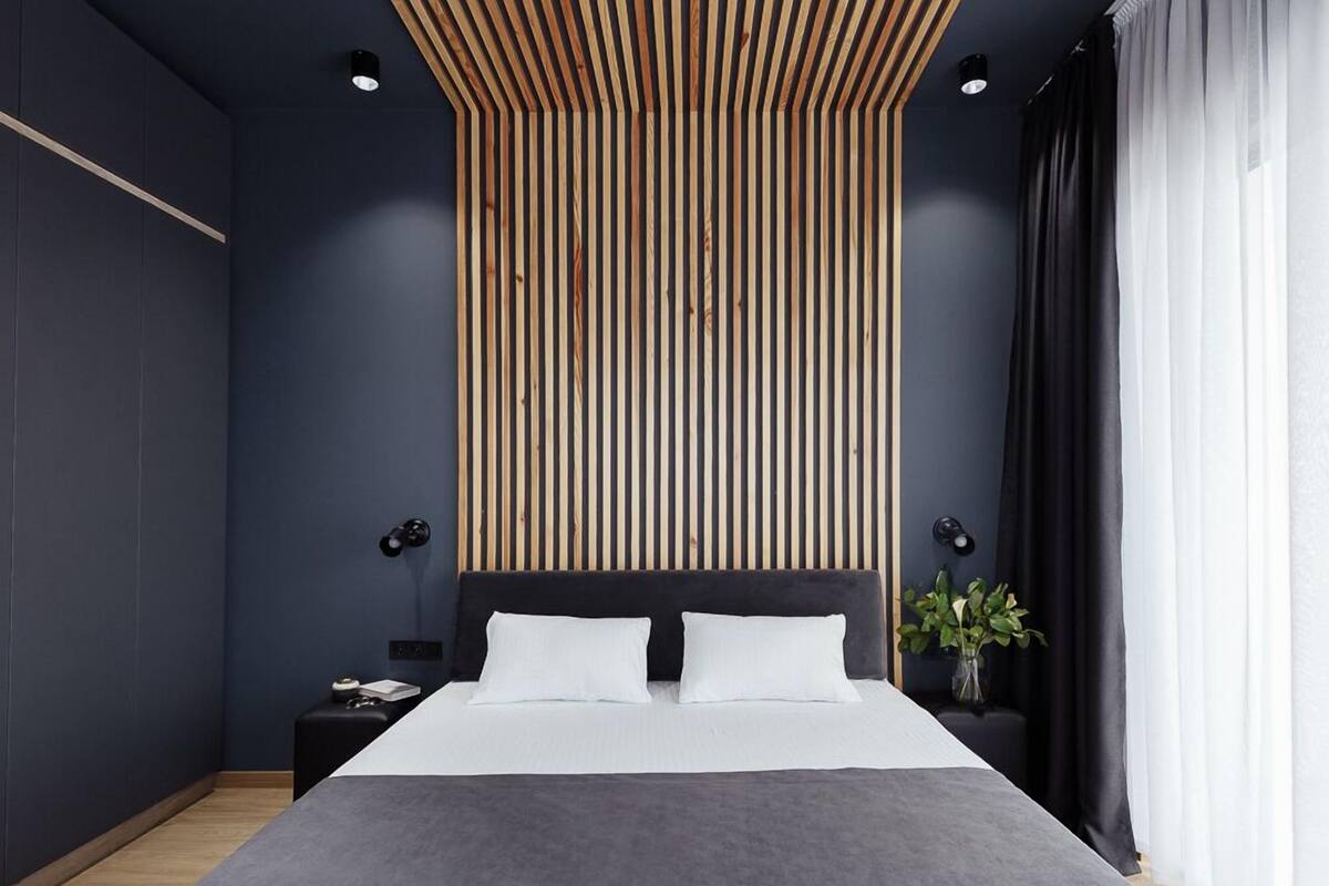 Une chambre moderne avec un mur bleu foncé, un plafond en lambris de bois, une tête de lit noire et une table de chevet avec une lampe.