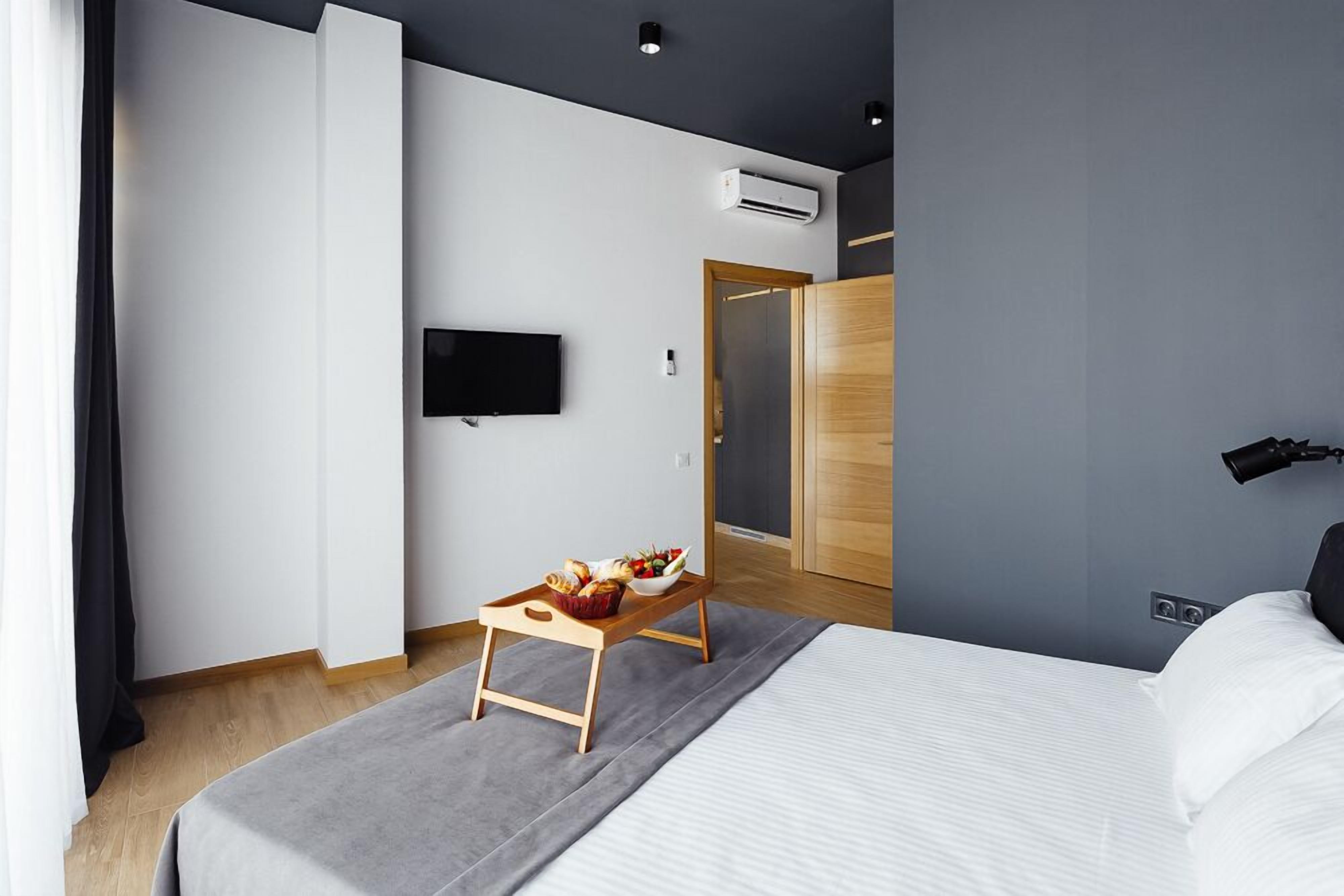 Een moderne hotelkamer met een bed, een flatscreen televisie aan de muur, een houten nachtkastje met een ontbijttafel en een garderobe met spiegel.