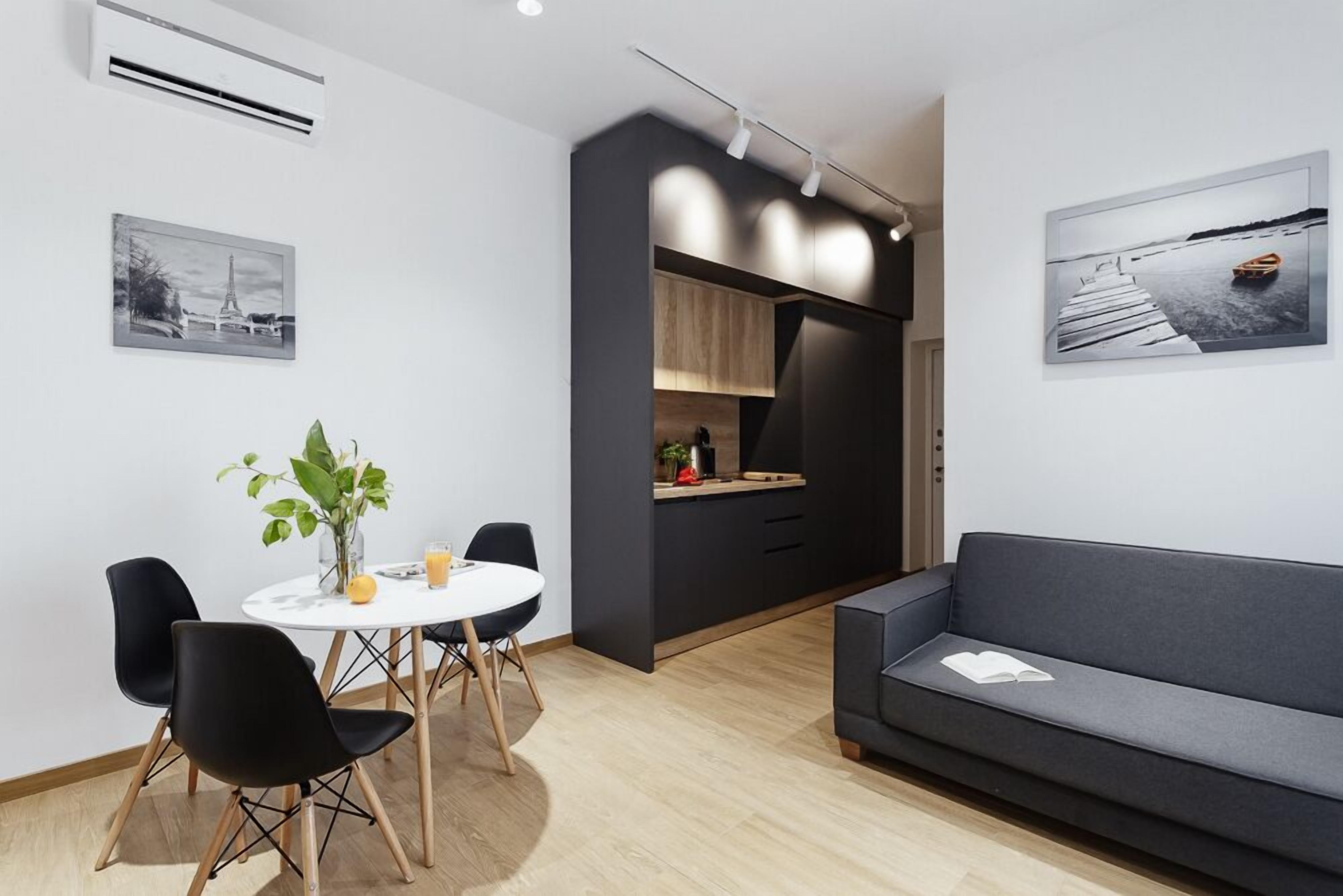 Una sala de estar moderna con un sofá gris, una mesa de comedor con sillas y una zona de cocina con armarios y encimera.