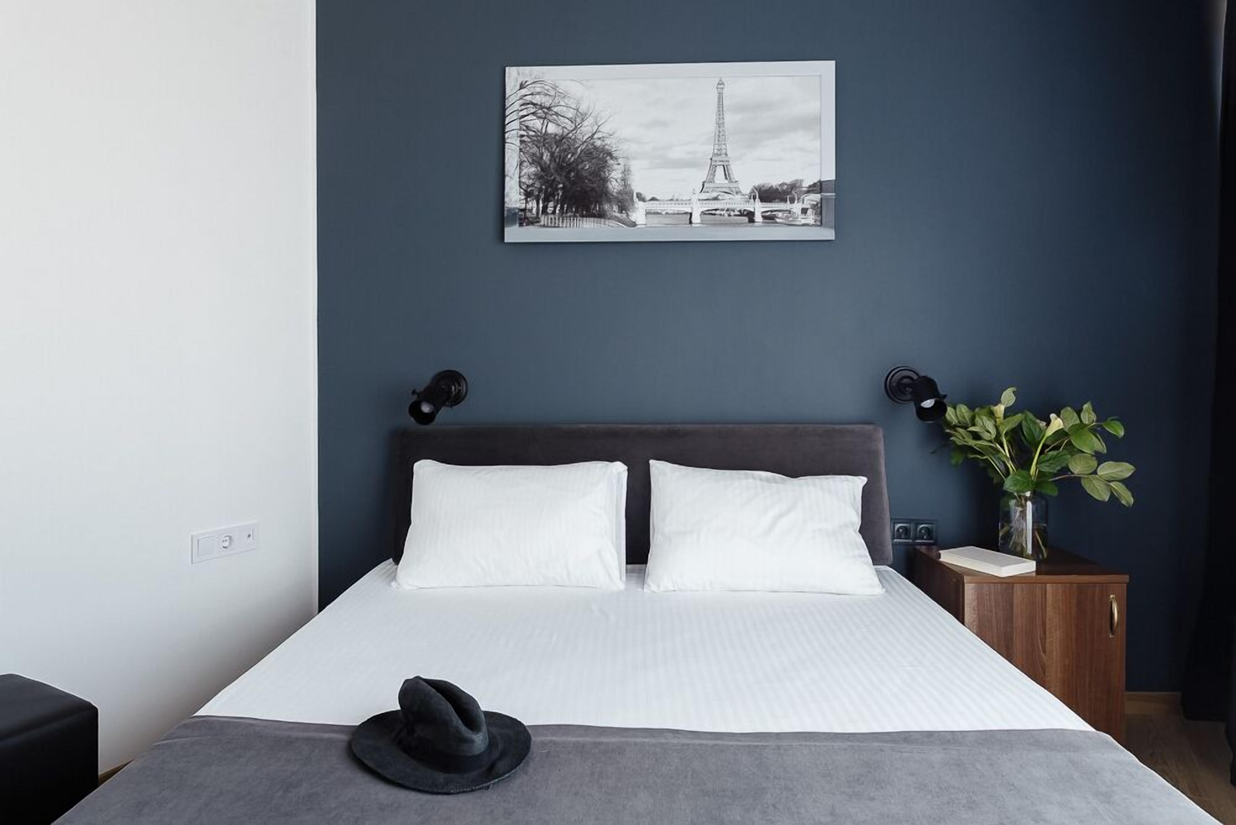 A neatly made bed with white linens, a dark headboard, and a black hat on the bed.