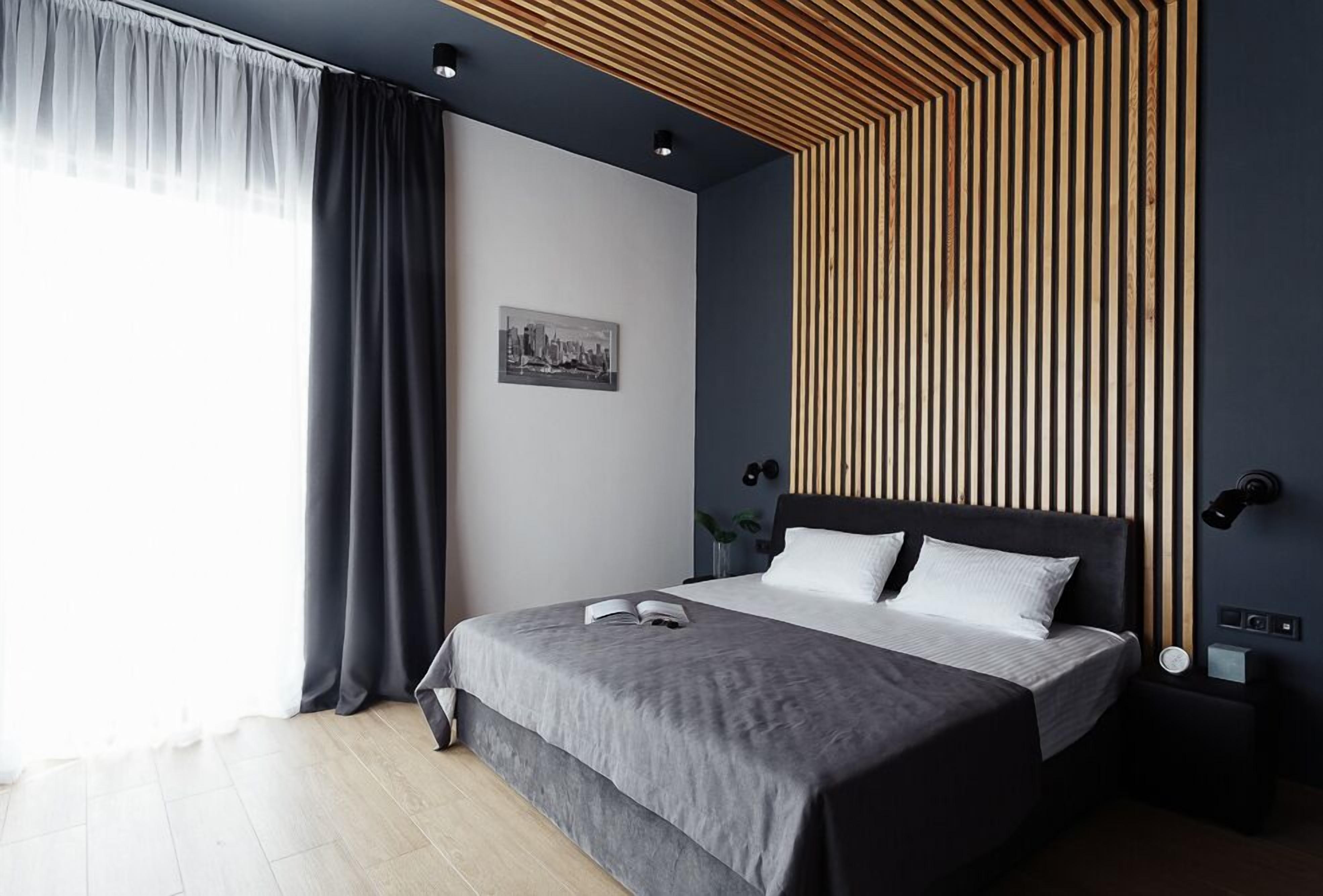 A modern bedroom with a large bed, a cityscape artwork on the wall, and a unique wooden slat ceiling design.