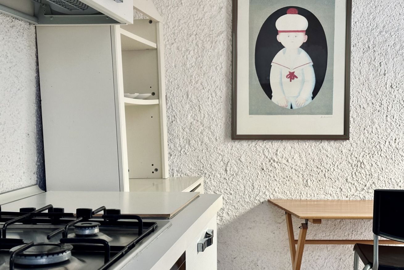 Een keuken met een gasfornuis, een wit kastje en een lijst met een kunstwerk aan de muur.