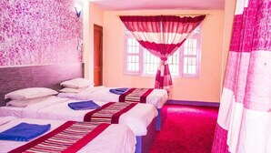 Habitación de hotel con tres camas, un ventilador de techo, una ventana con cortina roja y blanca, y alfombra rosa.
