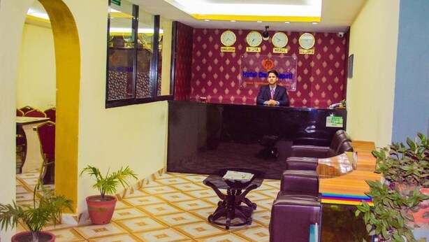 Zona de recepción de un hotel con mostrador para el personal, un sofá y plantas en macetas.