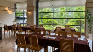 Un comedor con ventanas amplias, sillas de madera y mesas cubiertas con manteles oscuros.